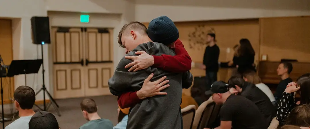 Young men embracing at church service